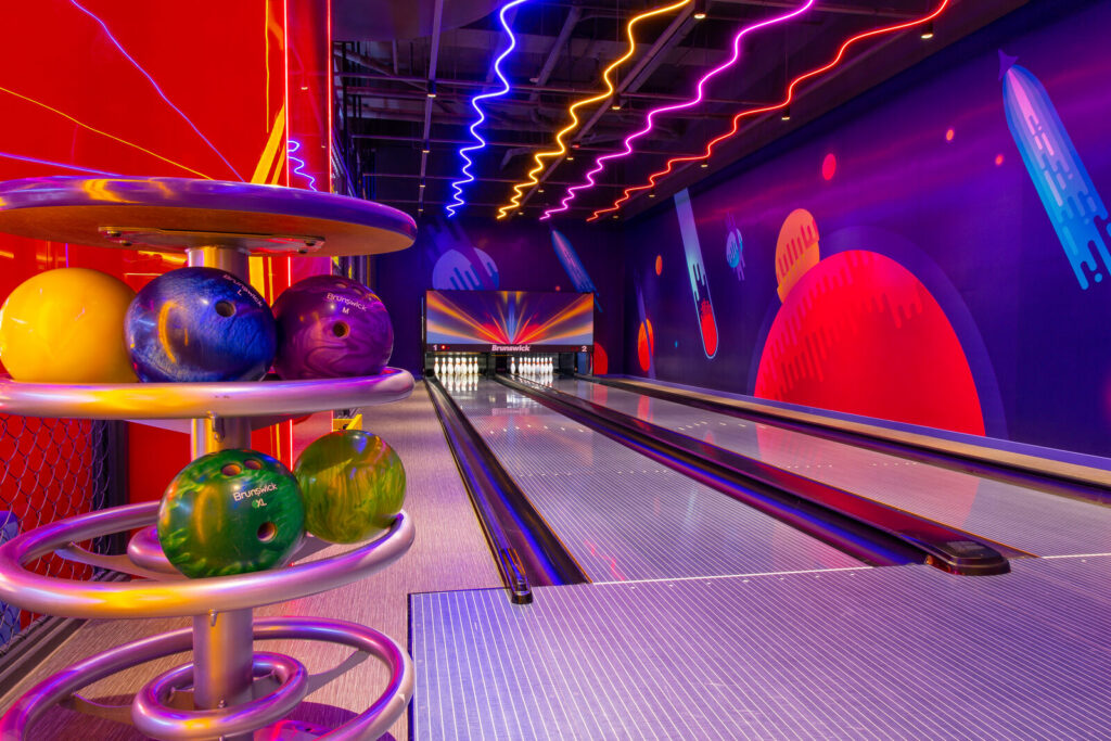 Circular house ball rack holding coloured rental bowling balls beside a lane